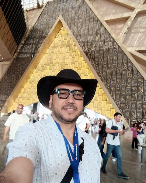 Selfie of Michael Sabry in front of the golden pyramid-shaped entrance wall of the Grand Egyptian Museum